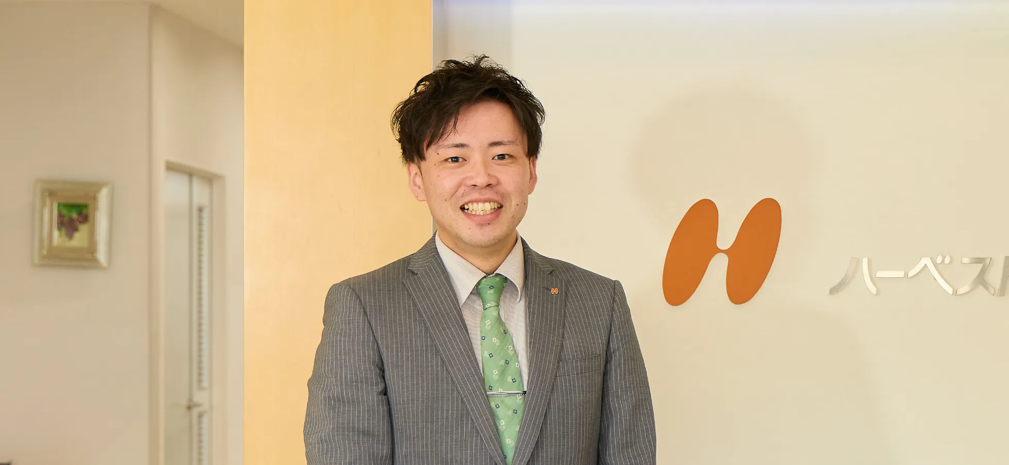 社名ロゴの前に立つK.T.さん