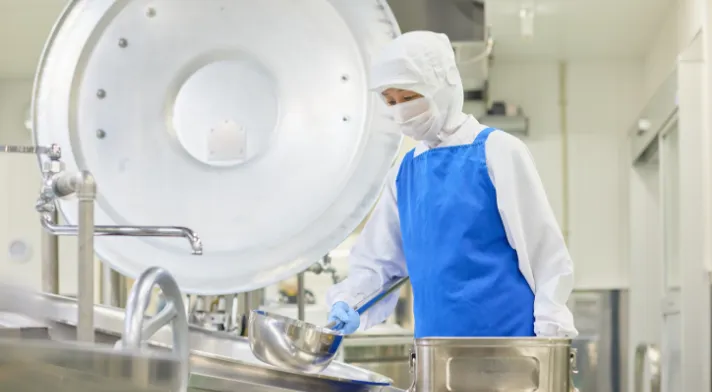 エプロンとゴム手袋をしてボウルを持つA.K.さん